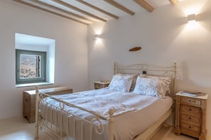 A bedroom with a bed, bedside tables, a window, and a wall-mounted light fixture. - Holiday Apartment 'Mrs Kalis Cottage' with Mountain View, Garden & Wi-Fi (ANDROS)