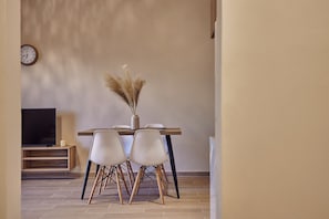 Un coin repas avec une table en bois, des chaises blanches et un vase décoré de plumes d’herbe de la pampa.