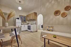 A modern kitchen with white appliances, a dining area with a wooden table and chairs, and a living area with a sofa and decorative wall art.