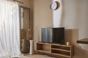 Un salon moderne avec un téléviseur posé sur un meuble en bois, une horloge murale et un vase décoratif orné de branches.