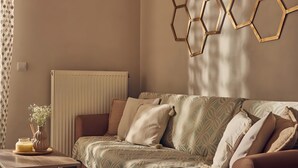 Uma sala de estar moderna com um sofá, uma mesa lateral com um vaso e uma vela, e um acessório de iluminação hexagonal fixado na parede.