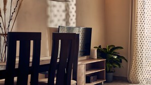 Uma área de refeições com uma mesa de madeira, cadeiras, uma televisão, um relógio e um vaso com planta.