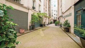 Un vialetto stretto con piante in vaso e persiane chiuse alle finestre.