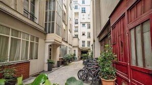 A narrow alleyway with buildings on either side, a red door on the right, and bicycles parked along the path. - Géranimus 163 : Heart of paris (Paris)