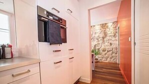 Cucina con mobili bianchi, forno a incasso e parete in pietra sullo sfondo.