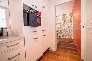 Une cuisine avec des armoires blanches, un four encastré et un mur en pierre en arrière-plan.