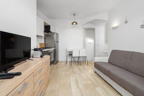 A modern kitchen with a flat-screen TV, wooden cabinets, and a dining area with chairs.