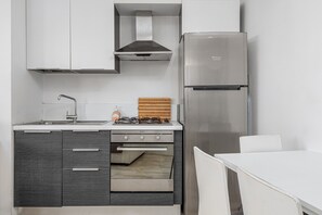 A compact kitchen with a gas stove, oven, stainless steel refrigerator, and white cabinetry.