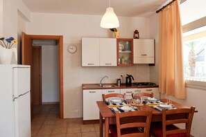 Une cuisine compacte avec des meubles blancs, une table à manger pour deux personnes et une suspension décorative.