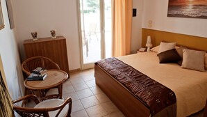 Ein Schlafzimmer mit einem Bett, einer Holzkommode, einem Korbstuhl und Blick ins Freie durch eine Glastür.