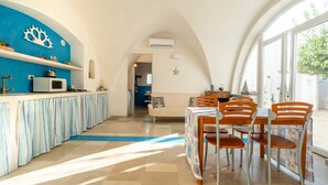 Een keuken met een blauwe wand, een wit plafond, en een eethoek met houten stoelen en een tafel.