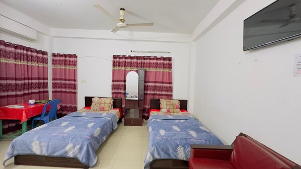 A room with two single beds, a desk with a chair, a TV mounted on the wall, and a ceiling fan. - Mohammadia Restaurant & Guest House (Dhaka)