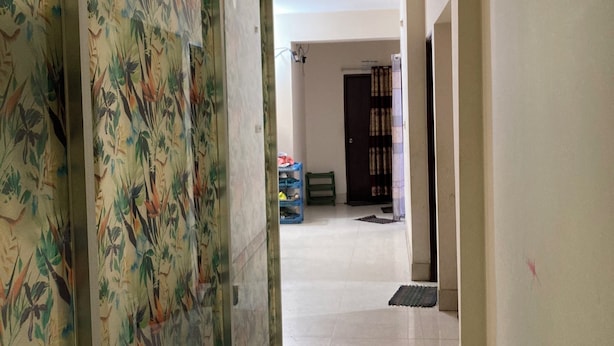 A hallway with a patterned door, a tiled floor, and a view into a room with a bed and a door in the background. - Mohammadia Restaurant & Guest House (Dhaka)
