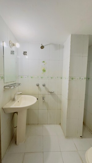 A bathroom with a white sink, a mirror, a shower, and tiled walls. - Mohammadia Restaurant & Guest House (Dhaka)