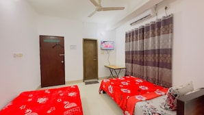 A hotel room with two single beds, a television, an air conditioning unit, a ceiling fan, and a curtain with a circular pattern. - Mohammadia Restaurant & Guest House (Dhaka)