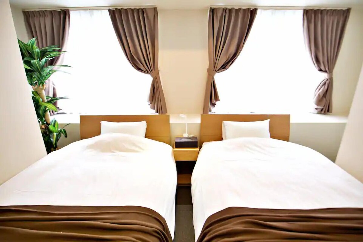 A mirrored room with two beds, brown curtains, a nightstand, and a potted plant.