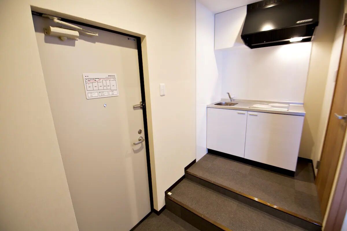 Una pequeña kitchenette con un lavamanos, armarios y una campana extractora negra.