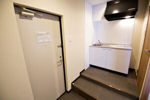 Una pequeña kitchenette con un lavamanos, armarios y una campana extractora negra.