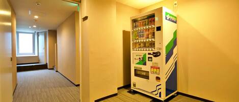 A vending machine in a hallway with carpeted floors and a door leading to another room.