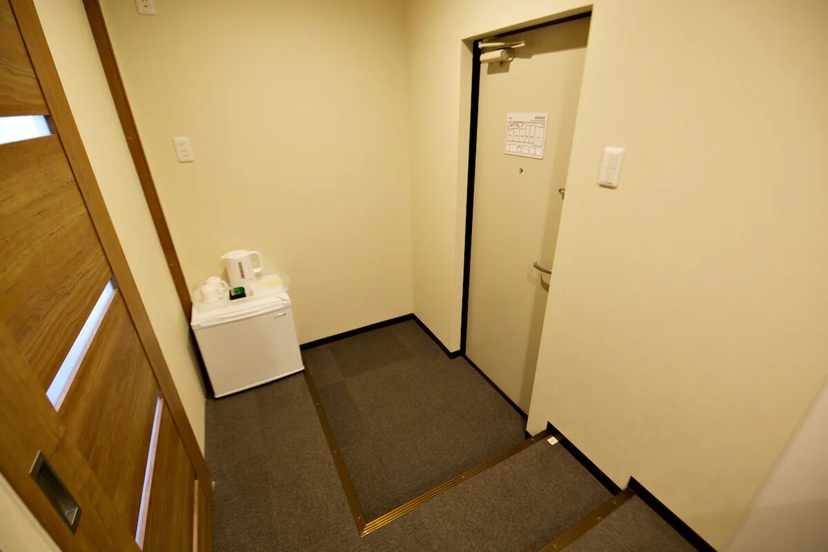 A narrow hallway with a carpeted floor, a white trash bin, and a door with a sign on it.