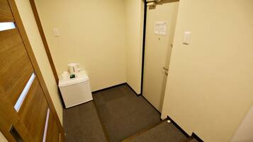A narrow hallway with a carpeted floor, a white trash bin, and a door with a sign on it.