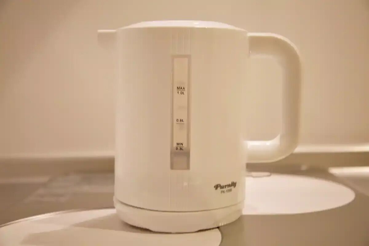 A white electric kettle with measurement markings on its side, placed on a white surface.