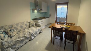 A compact living space with a kitchenette, a dining table with chairs, and a sofa with patterned cushions. - Alghero Lido sunny beach apartment ☀️ (Alghero)