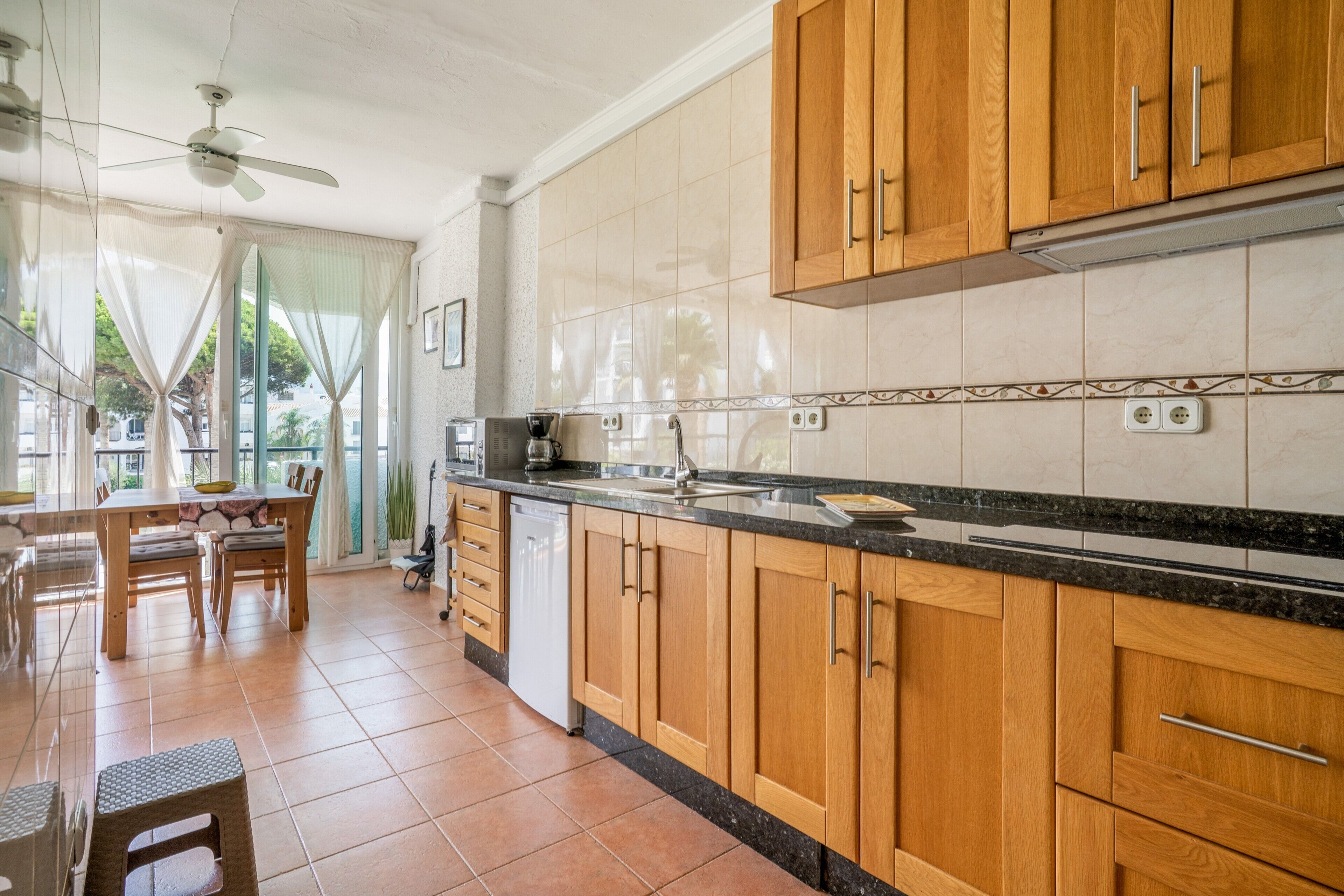 A kitchen with wooden cabinets, a black countertop, and a dining area with a table and chairs.