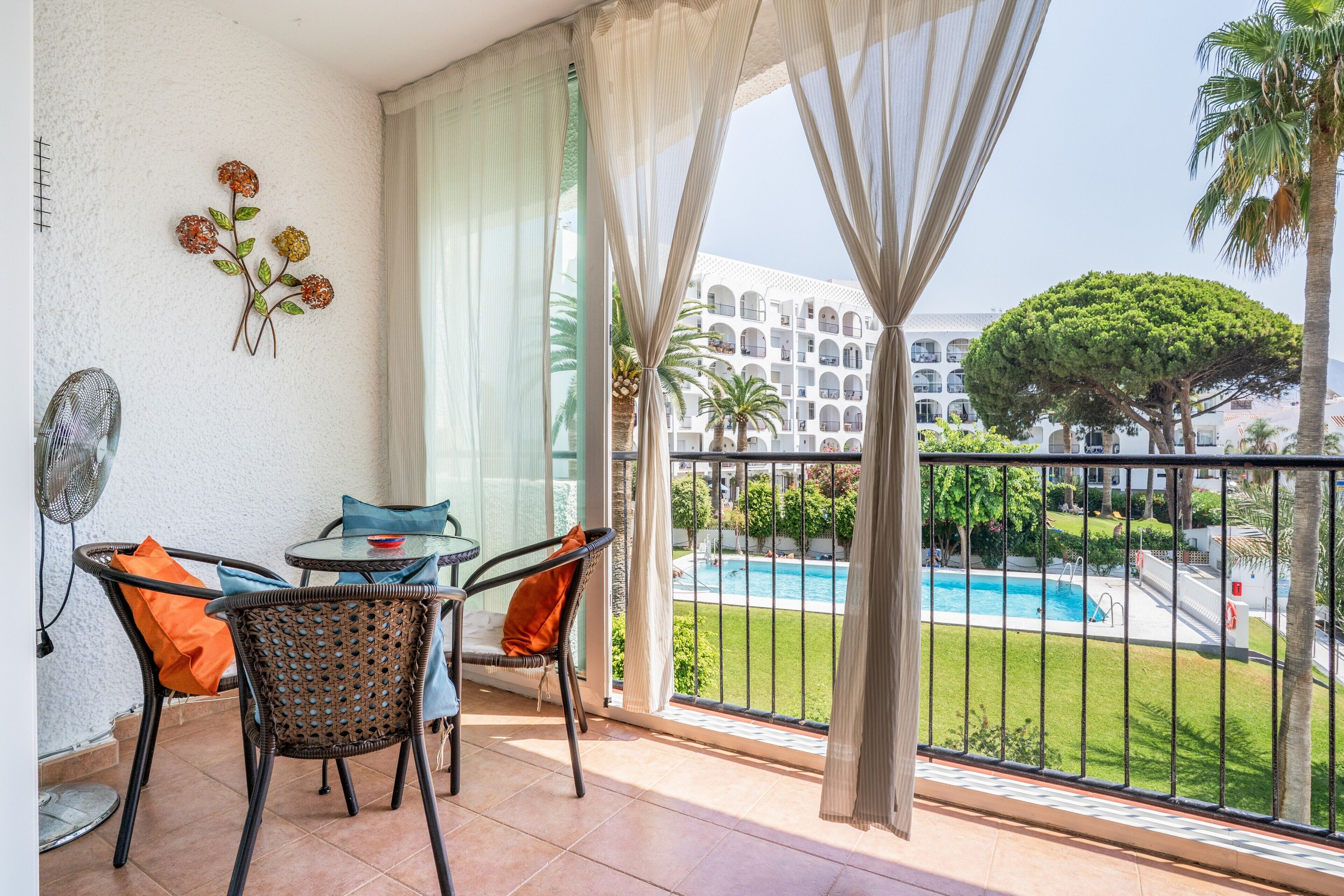 Varanda com mesa e cadeiras, piscina ao fundo e vista de um edifício com varandas.