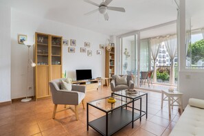 Una sala de estar moderna con un televisor de pantalla plana, dos sillones, una mesa de centro y un ventilador de techo.