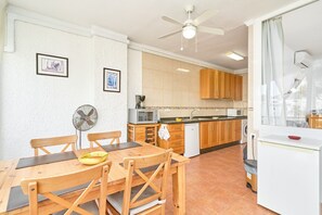 Une cuisine moderne avec des meubles en bois, une table à manger avec des chaises, un ventilateur de plafond et une fenêtre avec des rideaux.