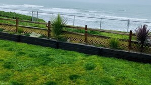 A coastal view with a grassy area, a wooden fence, and a metal railing overlooking the ocean.
