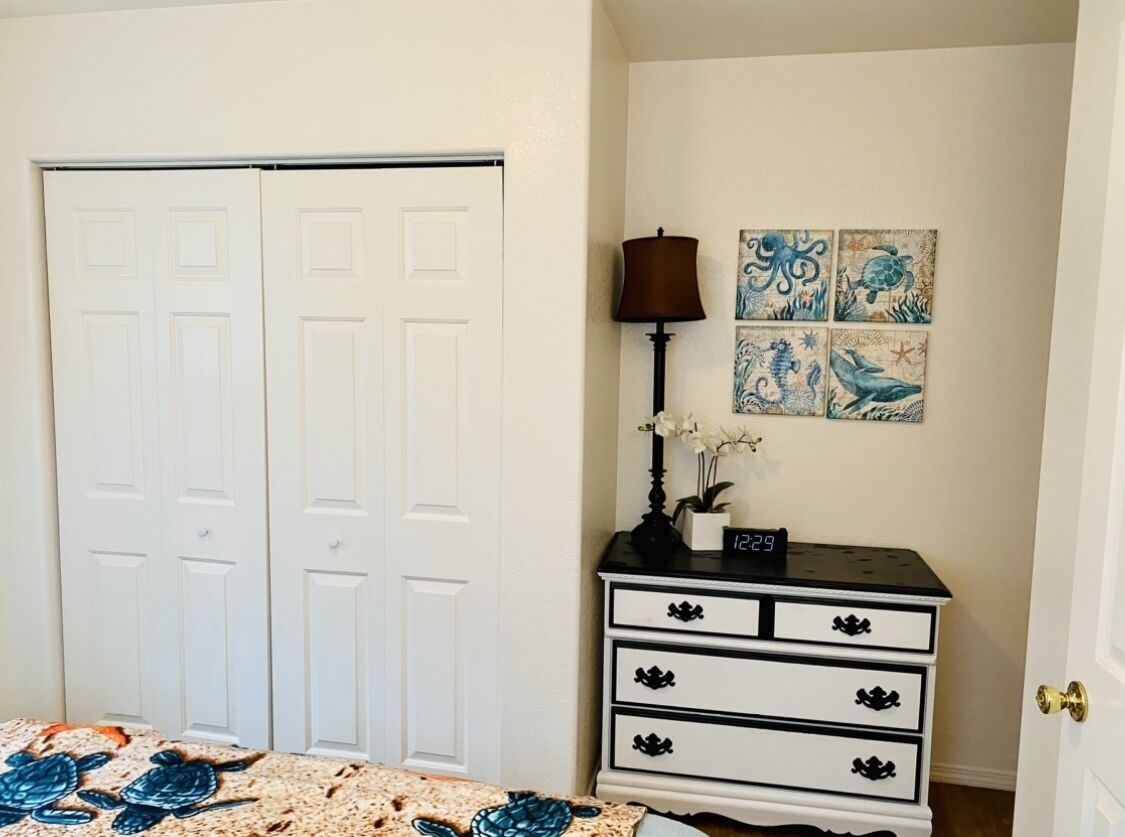 Quarto com porta de casal, mesa de cabeceira com abajur e decoração na parede.