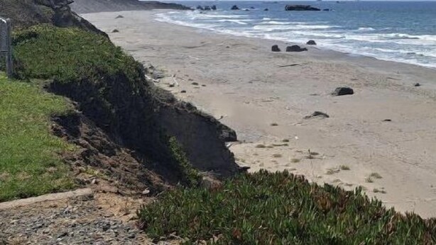 A coastal beach with a rocky cliff and a clear view of the ocean.