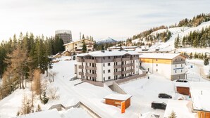 Een met sneeuw bedekte bergstad met moderne gebouwen, waaronder een meerlaags hotel met balkons en een skilift op de achtergrond.