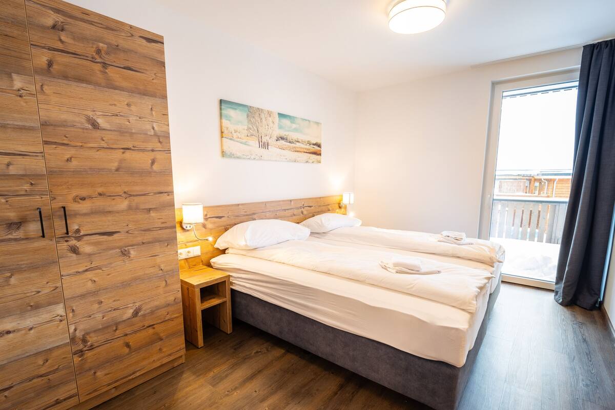 Ein Schlafzimmer mit einem Holfischschrank, einem Bett mit weißer Bettwäsche, einem Bild an der Wand und einem Balkon mit Aussicht.