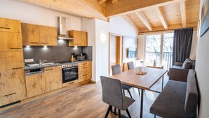 Een moderne keuken met houten kastjes, een inbouwoven en een eethoek met een tafel en stoelen.