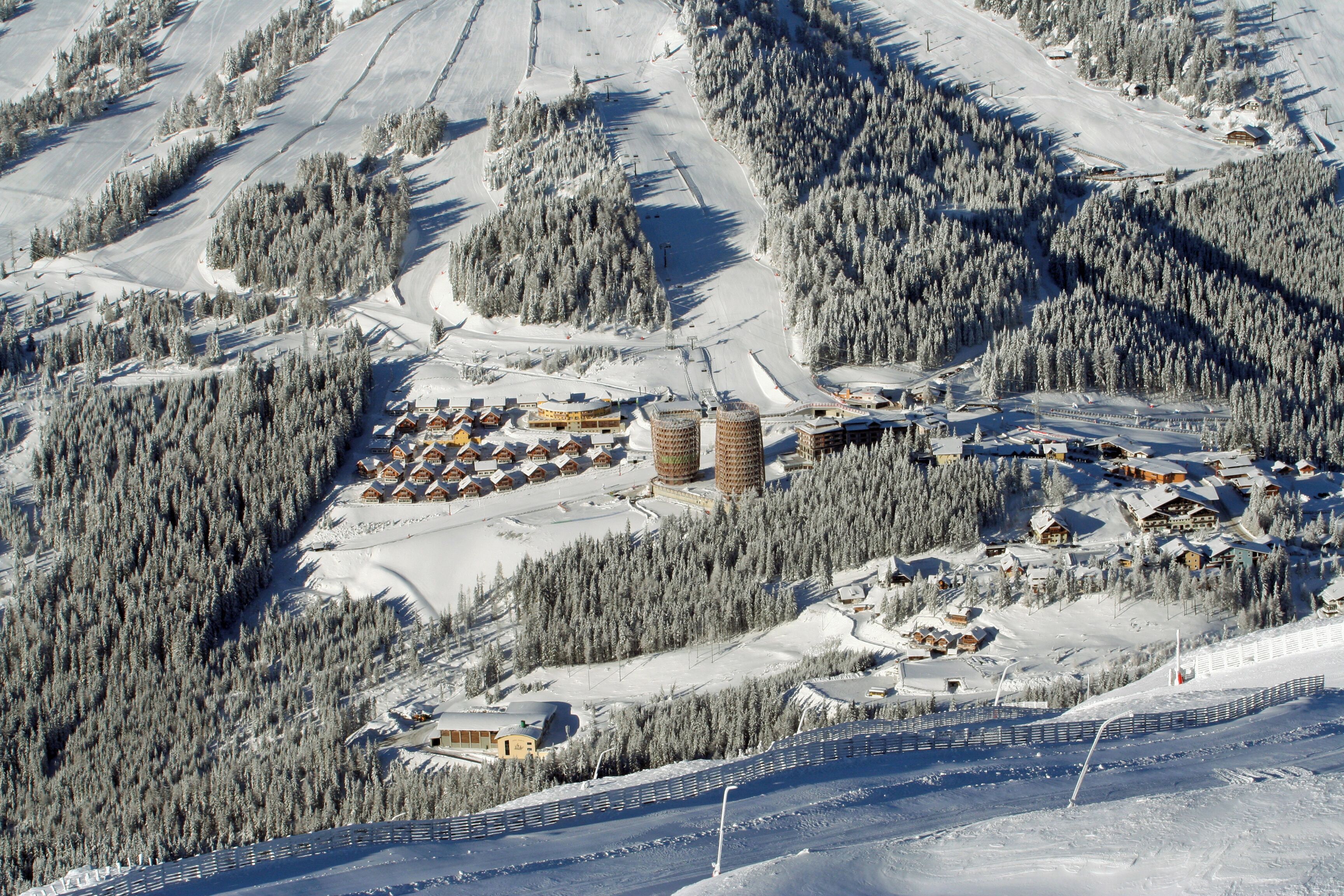 Ein verschneites Skigebiet mit Berghütten, einer Seilbahn und einem Berg im Hintergrund.