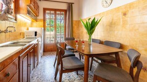 Une cuisine avec des meubles de rangement en bois, une table à manger avec des chaises, une horloge au mur et une fenêtre avec des rideaux.