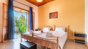 Une chambre à coucher avec un lit, une table de chevet, un banc et une vue sur la verdure par la fenêtre.
