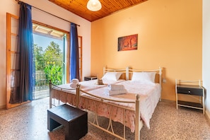 A bedroom with a bed, a bedside table, a bench, and a view of greenery through a window. - Holiday Home 'Princess House' with Private Terrace, Private Garden and Wi-Fi (Sidari)