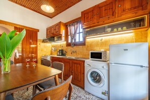 A kitchen with wooden cabinets, a washing machine, a refrigerator, and a dining table with chairs.