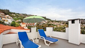 A rooftop terrace with two blue lounge chairs and a green umbrella, overlooking a hillside town. - Holiday Home "Casal Do Farrobo" with Sea View, Private Terrace & Wi-Fi (Funchal)