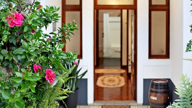 A wooden door with glass panels, a potted plant with pink flowers, a round wooden table, and a barrel. - Holiday Home "Casal Do Farrobo" with Sea View, Private Terrace & Wi-Fi (Funchal)