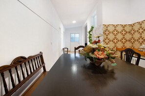 A dining area with a long table, chairs, a wooden headboard, and a floral centerpiece.