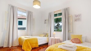 A hotel room with two beds, a small round table, a lamp, and a window with curtains. - Holiday Home "Casal Do Farrobo" with Sea View, Private Terrace & Wi-Fi (Funchal)