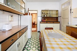 A compact kitchen with a dining area, featuring a checkered tablecloth, a refrigerator, and a microwave.