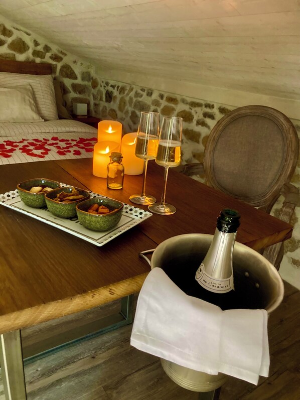 A cozy room with a wooden table set for a romantic dinner, featuring candles, glasses, and a bottle of champagne.