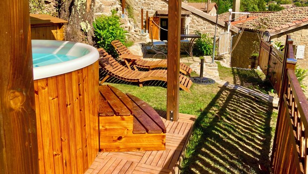Una terraza de madera con un jacuzzi, sillas de descanso y un edificio de piedra al fondo.
