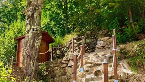 Una escalera de piedra con barandillas de metal, rodeada de vegetación y una estructura de madera.